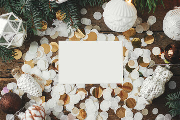 Empty greeting card and christmas vintage baubles, decorations, confetti and pine branches on rustic wood. Christmas card mock up flat lay. Space for text. Seasons greetings template