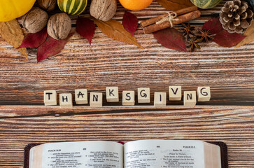 Thanksgiving word on wooden cubes with handwritten letters, open Holy Bible Book, and fall fruits...