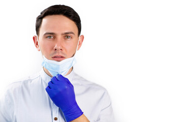 Handsome doctor takes off his mask. The guy puts on a protective mask. Handsome young man in a medical mask and gloves. Portrait of a doctor on a white background.