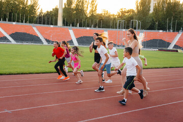 Fototapeta premium A large group of children, boys and girls, run and play sports at the stadium during sunset. A healthy lifestyle.