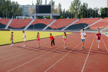 A large group of children, boys and girls, run and play sports at the stadium during sunset. A healthy lifestyle.