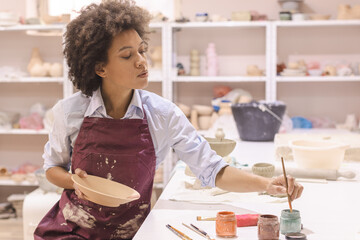 Portrait of afro american woman, pottery artist, workshop, painting clay dishwash. Creative crafts. Ceramic studio.