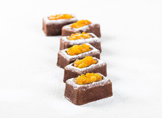 Rectangular chocolate savarin, small cake with a filling of tangerines in syrup, sprinkled with powdered sugar on a white background