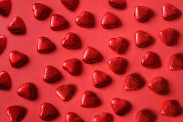 Pattern of romantic chocolate sweets as heart in red foil on red background. Valentine's day greeting card. Love concept.