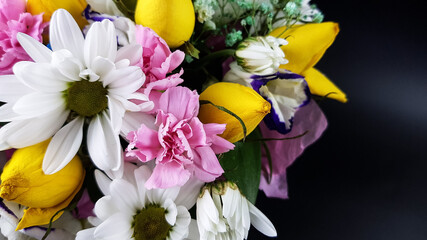 a colorful bouquet of multicolored yellow white and lilac flowers. composition of daisies roses chrysanthemums and carnations on a dark background