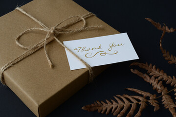 Present in a gift box, packed in eco-friendly kraft paper, and a thank you card on a dark blue...