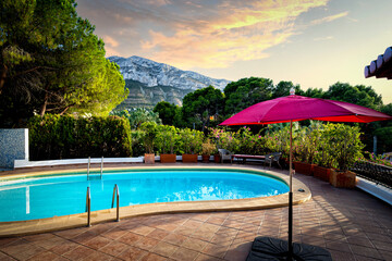 Blue pool under the pine trees with a red umbrella and a view of the mountain range.