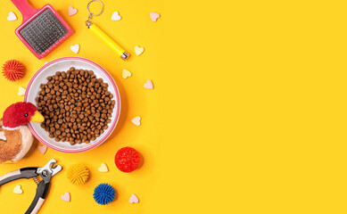 Cat dry food, grooming accessories and toys on a yellow background with space for design.