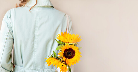 Eco-natural cotton reusable bag with sunflowers hanging on the shoulder of a girl in a light green jumpsuit, on a light background. Rear view. The concept of an ecological lifestyle and clothing