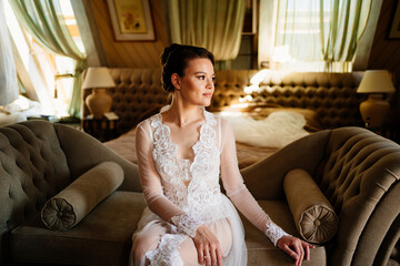 morning of bride. beautiful woman in lace robe sitting on couch in room. 