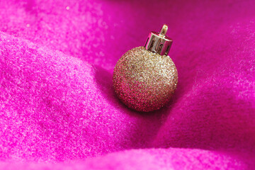 Creative Christmas background made with shiny golden ball ornament and soft magenta knitting. Minimal composition. Cozy and warm New Year's concept.