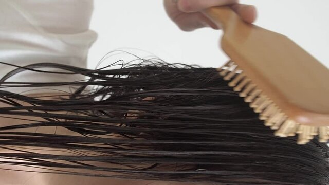 Woman brushing with combs tangled hair with conditioner after shower slow motion. Close up