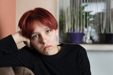 Fototapeta premium A teenage girl with red hair and complex character and a sad face is sitting at home, she quarreled with her friends and has no one to be friends with, she feels lonely