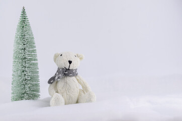 A white bear in the snow next to a snow-covered Christmas tree. A postcard with a knitted toy. Space for text.