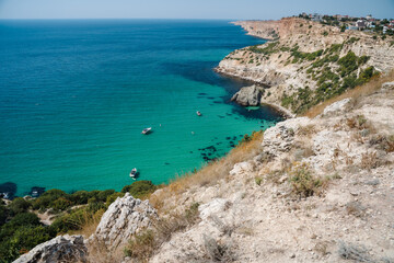 Fototapeta na wymiar Boats and yachts in the crystal clear azure sea on a sunny day. Cape Fiolent in Sevastopol. The concept of an ideal place for summer travel and relaxation