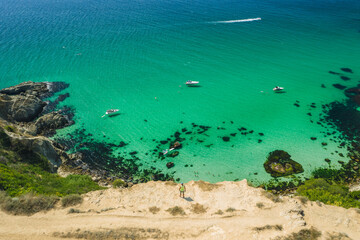 Man traveler on the edge in front of Bounty beach with crystal clear azure sea on a sunny day. Cape Fiolent in Sevastopol. Aerial view
