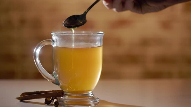 Slow motion footage of honey in a teaspoon being added to a steaming cup of ginger tea.