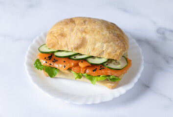 Fresh healthy salmon sandwich with lettuce and cucumber on white stone background. Breakfast snack