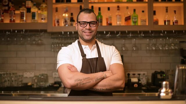 portrait of a confident smiling bartender at the bar in a restaurant with a tattoos on his hands