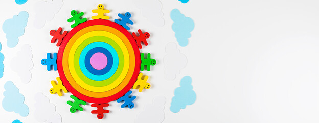 Banner. International Children's Day concept. Wooden toy children arround the rainbow on white background. Flat lay. Copy space.