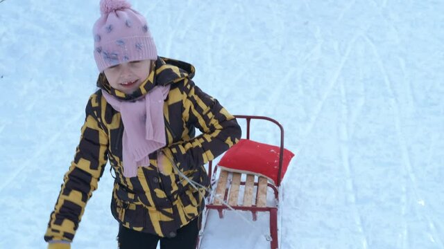 Sledding in a snowy park. A smiling child hold her sleigh and walk in the deep snow in the park.
