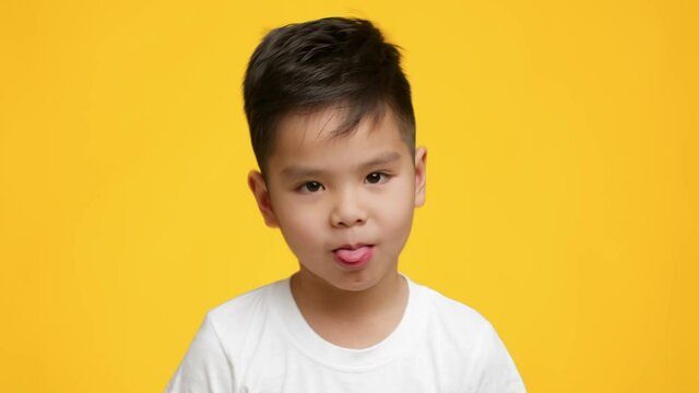 Little Japanese Boy Sticking Out Tongue Posing On Yellow Background