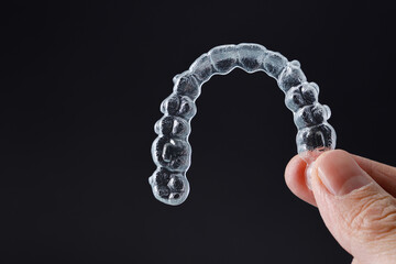 Hand holding one transparent retainer on black background. Invisalign orthodontics concept
