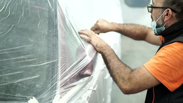 Auto mechanic preparing a car in a garage for painting. Protecting edges of a car in the workshop