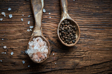 Salt and pepper on an ceramic spoon over wooden backround