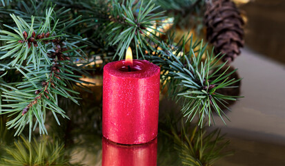 Close up of a red candle burning with fir branches on a gold background for a Merry Christmas or Happy New Year holiday theme