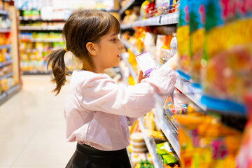 School aged girl in the supermarket looking for product she likes on the shelves and tries to chose from the large selection of colorful products.