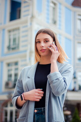 Business woman talking on the phone outdoors. Portrait of beautiful smiling girl in fashionable office clothes. Remote work