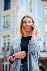 Business woman talking on the phone outdoors. Portrait of beautiful smiling girl in fashionable office clothes. Remote work