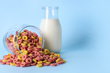 Glass with crunchy corn flakes rings and bottle of milk on color background