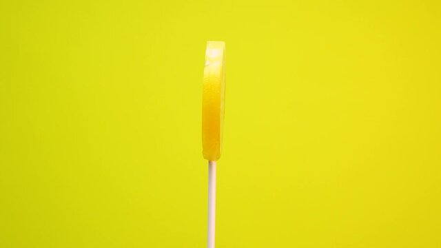 Fruit lollipop on a yellow background. Caramel Lemon candy is spinning