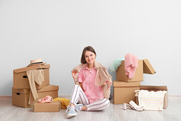 Young woman with clothes and wardrobe boxes near light wall