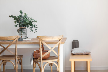 Dining table with eucalyptus branches in vase near light wall
