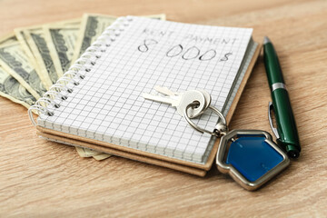 Notebook, pen, money and key with house shaped keychain on wooden background, closeup