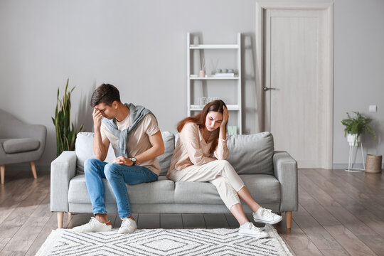Upset young couple after quarrel sitting on sofa at home