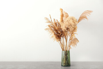 Vase with beautiful dry reeds on wooden table against white background