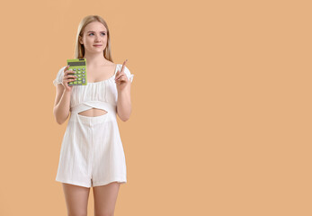 Young blonde woman with calculator pointing at something on beige background