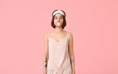 Young woman in pajamas and with chewing gum on color background