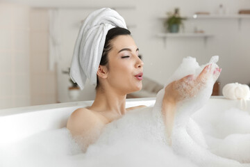 Relaxed young woman blowing foam in bathtub