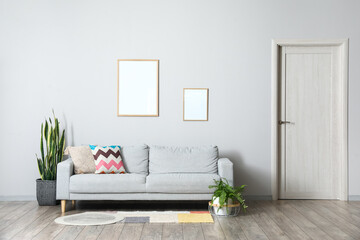 Interior of light living room with grey sofa and blank frames