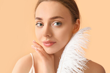 Beautiful young woman with soft feather on color background