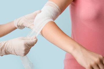 Doctor bandaging patient hand on color background, closeup