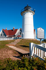 Nobska Light historic architectural landscape over the green hill with rosehip bush on blue sky background.