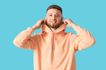Fototapeta premium Casual fashion and comfortable style, young man in peach hoodie on blue background