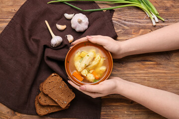 Woman holding bowl with delicious dumpling soup on wooden background, closeup
