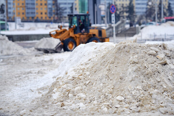 Snowdrift, pile of snow on sidewalk and municipal snow removal loader on background. Snow and ice...